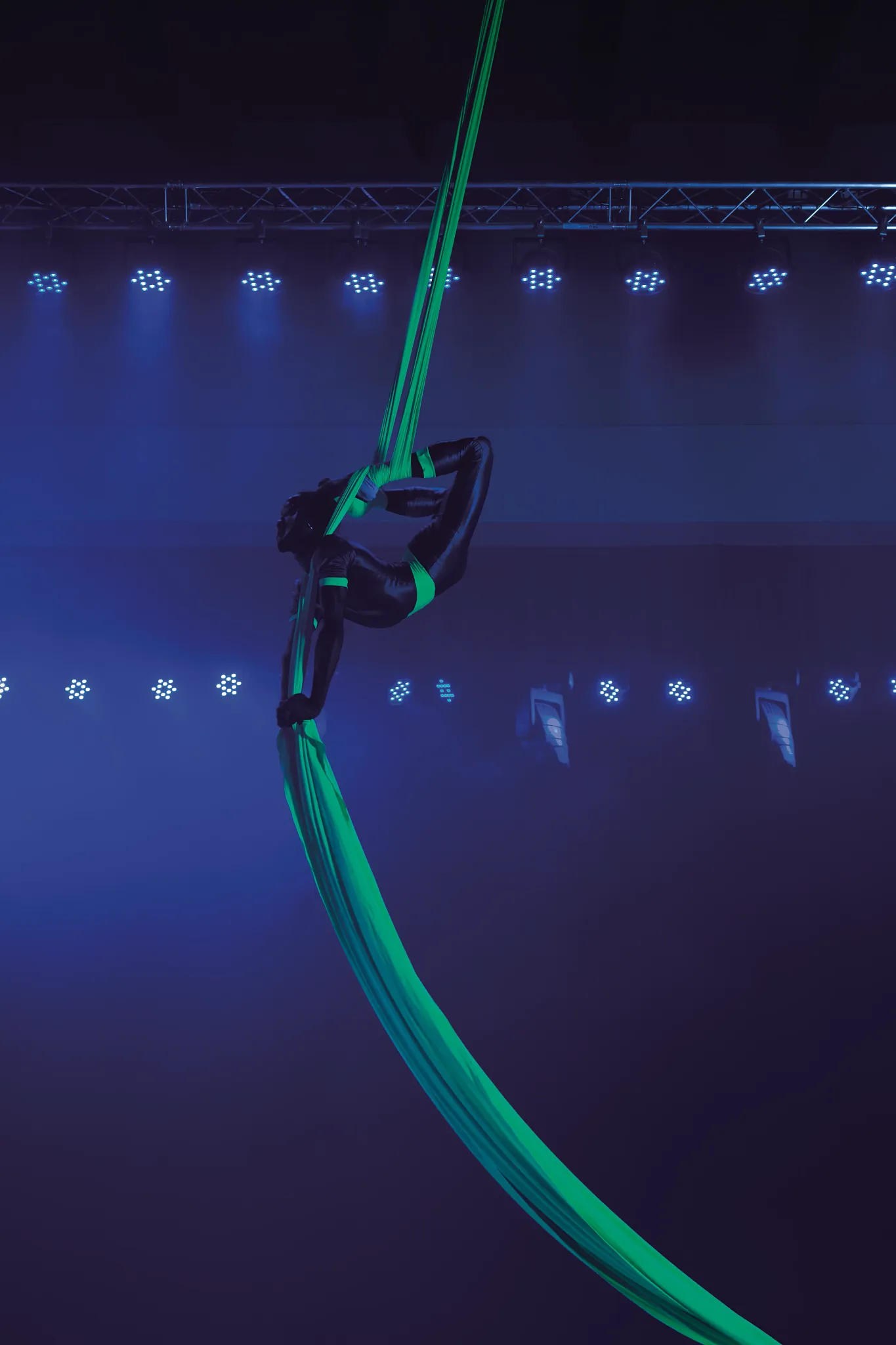Female acrobat performing at a nightclub wearing dark clothing with highlights to glow green in blacklight